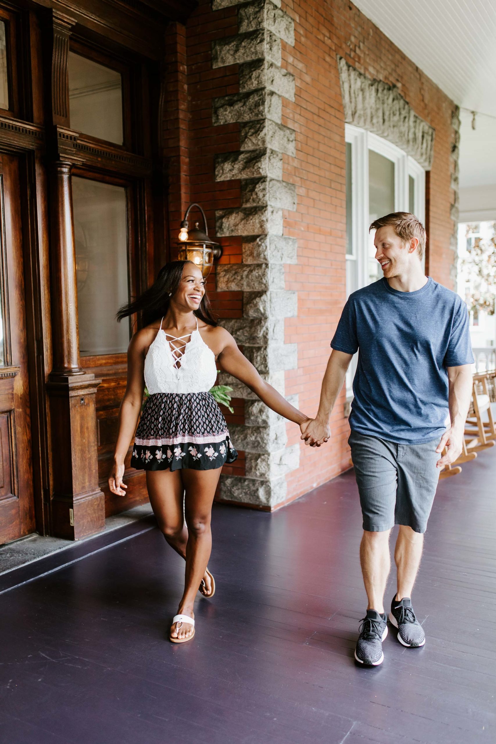 couple walking in front of house while holding hands and smiling